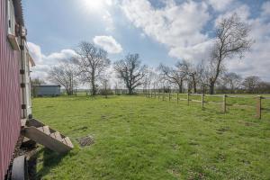 a field with a fence and trees in the background at Thyme Shepherds Hut Boundary Farm Air Manage Suffolk in Woodbridge