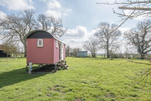 a small red shed sitting in a field at Thyme Shepherds Hut Boundary Farm Air Manage Suffolk in Woodbridge