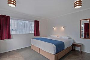 a bedroom with a large bed with red curtains at Comfort Inn Westshore Beach in Napier