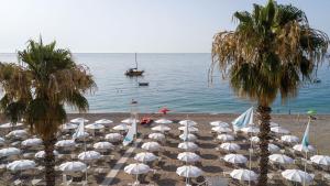 a beach with white umbrellas and palm trees and a boat at Albatros Beach Hotel in Letojanni