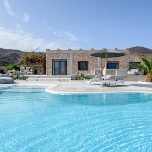 a large swimming pool with an umbrella in front of a house at Villa Beltramo Santorini 2 bedroom private pool villa in Foinikiá