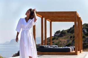 eine Frau in einem weißen Kleid steht neben einem Bett in der Unterkunft Pristine Seaview Villa , with 5-Star Resort Access in Faliraki