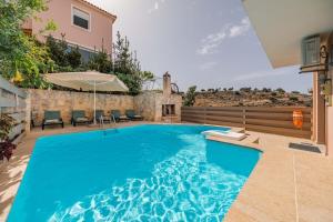 una piscina en un patio trasero con sillas y sombrilla en Mikra Anogia Villas, en Rethymno