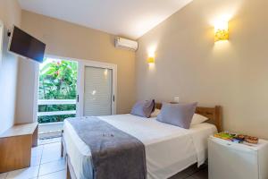 a bedroom with a white bed and a window at Pousada Toca da Praia in Maresias