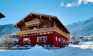 a red building with a wooden roof in the snow at APARTMENT SONNBLICK Kaprun Salzburg - incl Zell am See-Kaprun Summercard in Kaprun