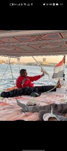 un hombre sentado en la parte superior de un barco en el agua en My Dream Nile Felucca en Asuán