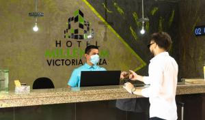 Due uomini in piedi al bancone con un uomo che indossa una maschera. di Hotel Victoria Plaza Millenium a Cúcuta