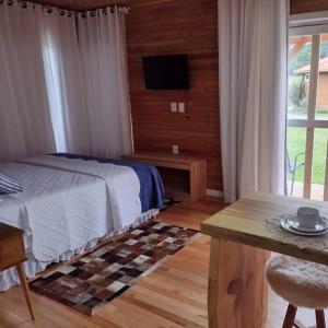 a bedroom with a bed and a television and a table at Pousada caminhos do mel in Urubici
