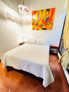 a bedroom with a white bed with a painting on the wall at Hostal Colina de Lluvia in Filandia