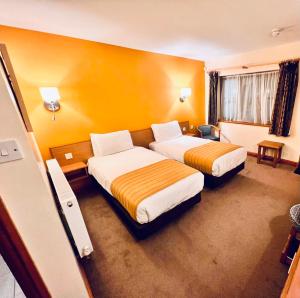 two beds in a hotel room with yellow walls at Tollgate Hotel & Leisure in Stoke on Trent