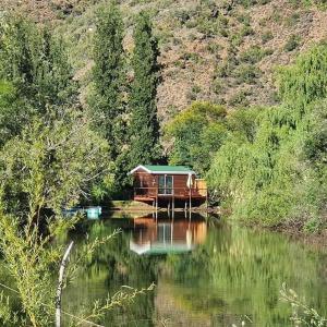 a house sitting on the side of a river at Old Mill Lodge, Seasonal Working Ostrich Farm & Restaurant, Oudtshoorn in Oudtshoorn