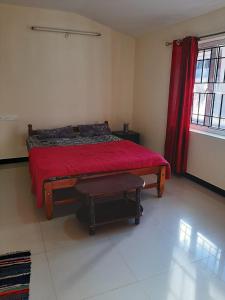a bedroom with a bed with a red blanket and a stool at jack N jill holidays inn in Ooty