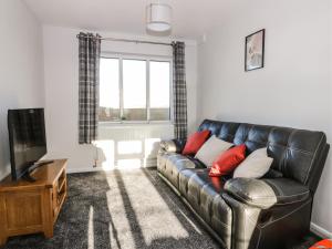 a living room with a leather couch and a television at 1 Woodhouse Cottages in Hull