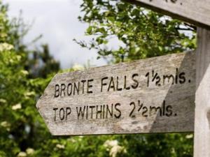 un signo de madera con las palabras bronceador cae himnos dentro de las advertencias en Leeming Wells, en Haworth