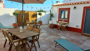 eine Terrasse mit einem Holztisch, Stühlen und einem Sonnenschirm in der Unterkunft Cantinho de Milfontes in Vila Nova de Milfontes