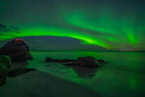 an aurora over a beach with rocks in the water at Feriehus med flott havutsikt ved Hauklandstranden in Leknes