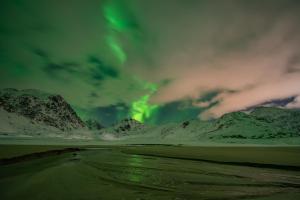 an aurora in the sky over a snowy mountain range at Feriehus med flott havutsikt ved Hauklandstranden in Leknes