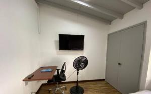 a room with a white wall with a desk and a fan at Apartamento cerca al centro comercial Santafé A105 By Roots Rentals in Medellín