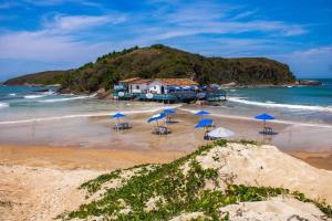 a beach with blue and white umbrellas and the ocean at Apartamento rústico in Cabo Frio