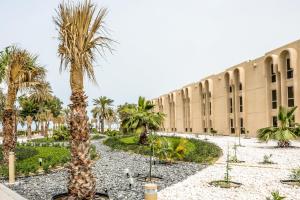 a large palm tree in front of a large building at Dhafra Beach Hotel - Pet Friendly in Jebel Dhanna