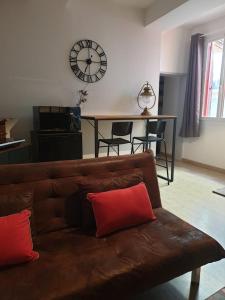 a brown couch in a living room with a clock on the wall at Suite privé dans maison de village in Soual