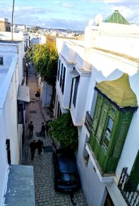 Une allée avec des bâtiments blancs et un bâtiment vert dans l'établissement Dar el médina, à Tunis