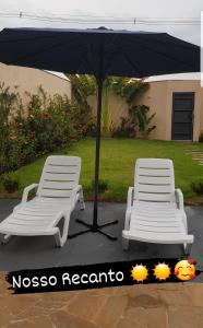 two white chairs and an umbrella on a patio at Casa Temporada Nosso Recanto Piscina aquecimento Solar in Olímpia