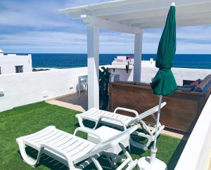 zwei weiße Stühle und ein Sonnenschirm auf einer Terrasse mit Meerblick in der Unterkunft BAHIA LA SANTA APARTMENTS LANZAROTE in La Santa