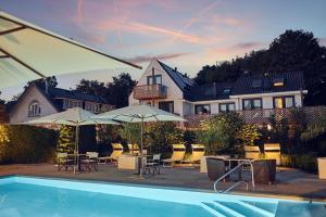 a swimming pool with tables and umbrellas and a house at Badhotel Renesse in Renesse