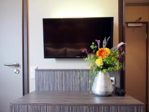 eine Vase voller Blumen auf einem Tisch mit einem TV in der Unterkunft Myhotel in Künzelsau