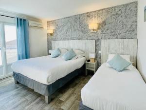 two beds in a hotel room with blue pillows at Hotel Les Palmiers En Camargue in Saintes-Maries-de-la-Mer
