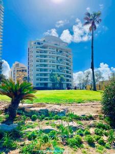 a tall building with palm trees and a grass field at Royal King David Apartment in Netanya