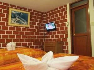 a room with two beds and a tv on a brick wall at Hostal Encanto Machupicchu in Machu Picchu