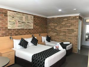 2 camas en una habitación con una pared de ladrillo en Jumbuck Motor Inn, en Tenterfield