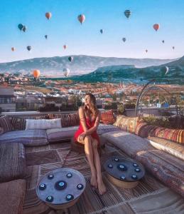 a woman in a red dress sitting on a ledge with hot air balloons at Caravanserai Inn Hotel in Goreme