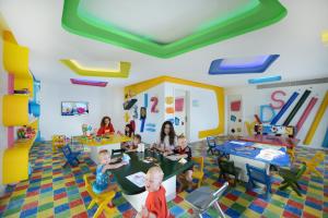 Pickalbatros Aqua Blu Resort - Hurghada في الغردقة: مجموعة من الأطفال يجلسون على الطاولات في غرفة لعب