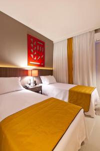 a hotel room with two beds and a red painting at San Diego Suites Veredas Sete Lagoas in Sete Lagoas