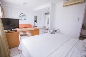 Praia do Canto Apart Hotel في فيتوريا: غرفة نوم بسرير ابيض وتلفزيون