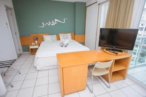 a bedroom with a bed and a desk with a television at Praia do Canto Apart Hotel in Vitória