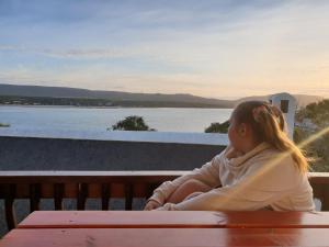 a young girl sitting on a bench looking at the water at Luxury Breede River View at Witsand- 300B Self-Catering Apartment in Witsand