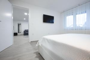 a white bedroom with a bed and a tv at Apartmani Dora in Požega