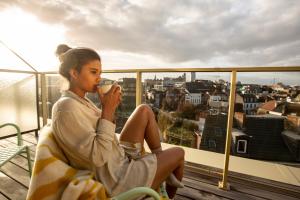 une femme assise sur un balcon buvant une tasse de café dans l'établissement Yalo Urban Boutique Hotel Gent, à Gand