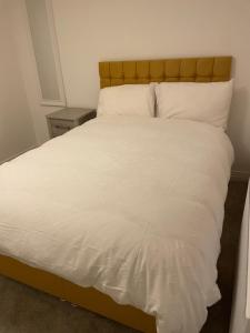 een groot bed met witte lakens en een houten hoofdeinde bij A luxurious 2-Bedroom flat in Rugby. in Rugby