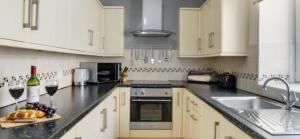 Una cocina con gabinetes blancos y un fregadero con copas de vino. en Anchor Point, en Seahouses