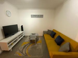 uma sala de estar com um sofá amarelo e uma televisão de ecrã plano em Marie’s Serviced Apartment 2 bed Olivier Court em Bedford