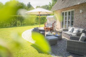 a patio with a couch and an umbrella and chairs at Ferienhaus Koellers Hus in Sankt Peter-Ording