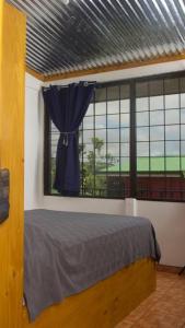 a bedroom with a bed and a window with a blue curtain at Basecamp Arenal in Tronadora