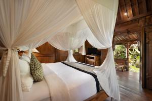 een slaapkamer met een wit bed en gordijnen bij Madani Antique Villas in Ubud