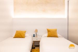 2 Betten in einem Zimmer mit weißen Wänden und gelben Kissen in der Unterkunft La Casa del Alfarero by Cadiz Time in Cádiz
