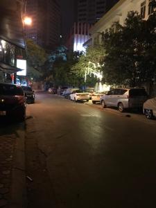 Una calle de la ciudad por la noche con coches aparcados en la calle en Hoàng Gia Hotel Nhân Hòa, en Hanói